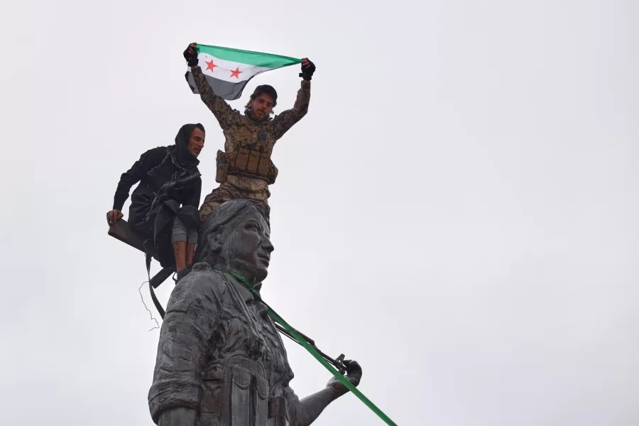 Syrian government soldiers wave a Syrian flag after climbing atop a statue of a female Kurdish fighter, following the takeover of the town from U.S.-backed Syrian Democratic Forces (SDF) during an ongoing push against Kurdish-led forces, in Tabqa, eastern Syria, Sunday, Jan. 18, 2026. (AP Photo/Omar Albam)