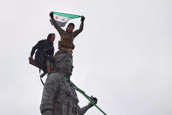 Syrian government soldiers wave a Syrian flag after climbing atop a statue of a female Kurdish fighter, following the takeover of the town from U.S.-backed Syrian Democratic Forces (SDF) during an ongoing push against Kurdish-led forces, in Tabqa, eastern Syria, Sunday, Jan. 18, 2026. (AP Photo/Omar Albam)