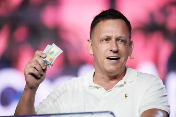 FILE – Peter Thiel, co-founder of PayPal and Palantir, offers a pair of hundred dollar bills to attendees during a keynote address at the Bitcoin Conference, April 7, 2022, in Miami Beach, Fla. (AP Photo/Rebecca Blackwell, File)