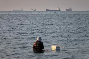 A person sits on shallow water as cargo and commercial vessels are anchored in the Strait of Hormuz off Bandar Abbas, Iran, Monday, June 8, 2026. (Amirhosein Khorgooi/ISNA via AP)