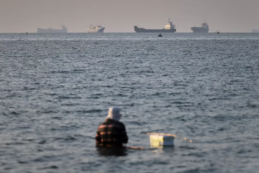 A person sits on shallow water as cargo and commercial vessels are anchored in the Strait of Hormuz off Bandar Abbas, Iran, Monday, June 8, 2026. (Amirhosein Khorgooi/ISNA via AP)