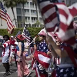 Participants carrying American flags join the festivities during the Independence Day Parade march along Main Street in Santa Monica, Calif. on Friday, July 4, 2025. (AP Photo/Richard Vogel)